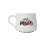 A white ceramic coffee mug featuring a retro-style illustration of a red vintage camper van parked in front of a mountain range with pine trees and a red sun.