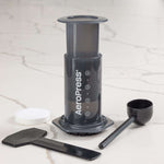 AeroPress coffee maker with scoop and stirrer on a marble counter