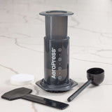 AeroPress coffee maker with scoop and stirrer on a marble counter