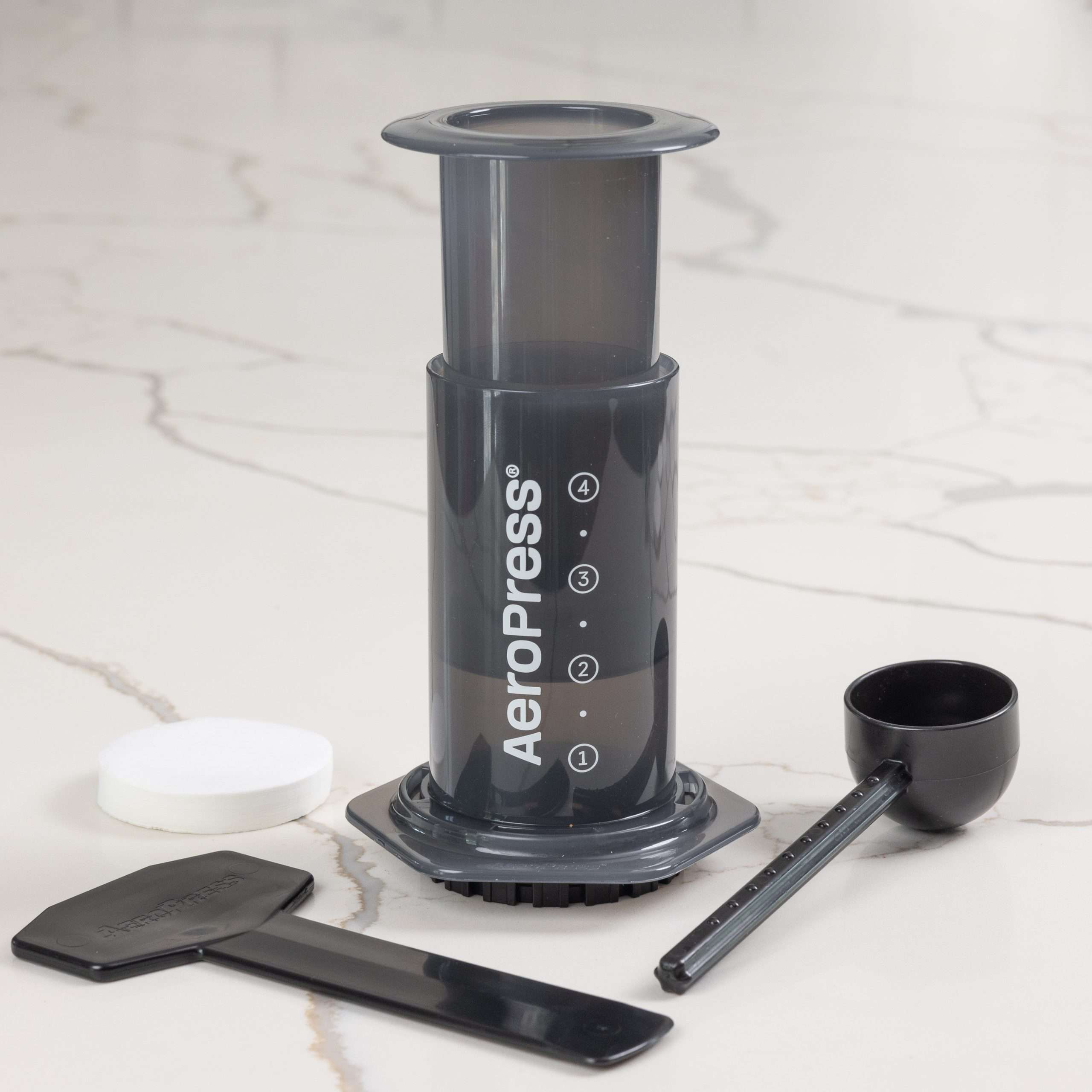 AeroPress coffee maker with scoop and stirrer on a marble counter