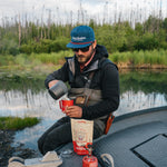 Man brewing Kaladi coffee on a boat beside an Alaska river