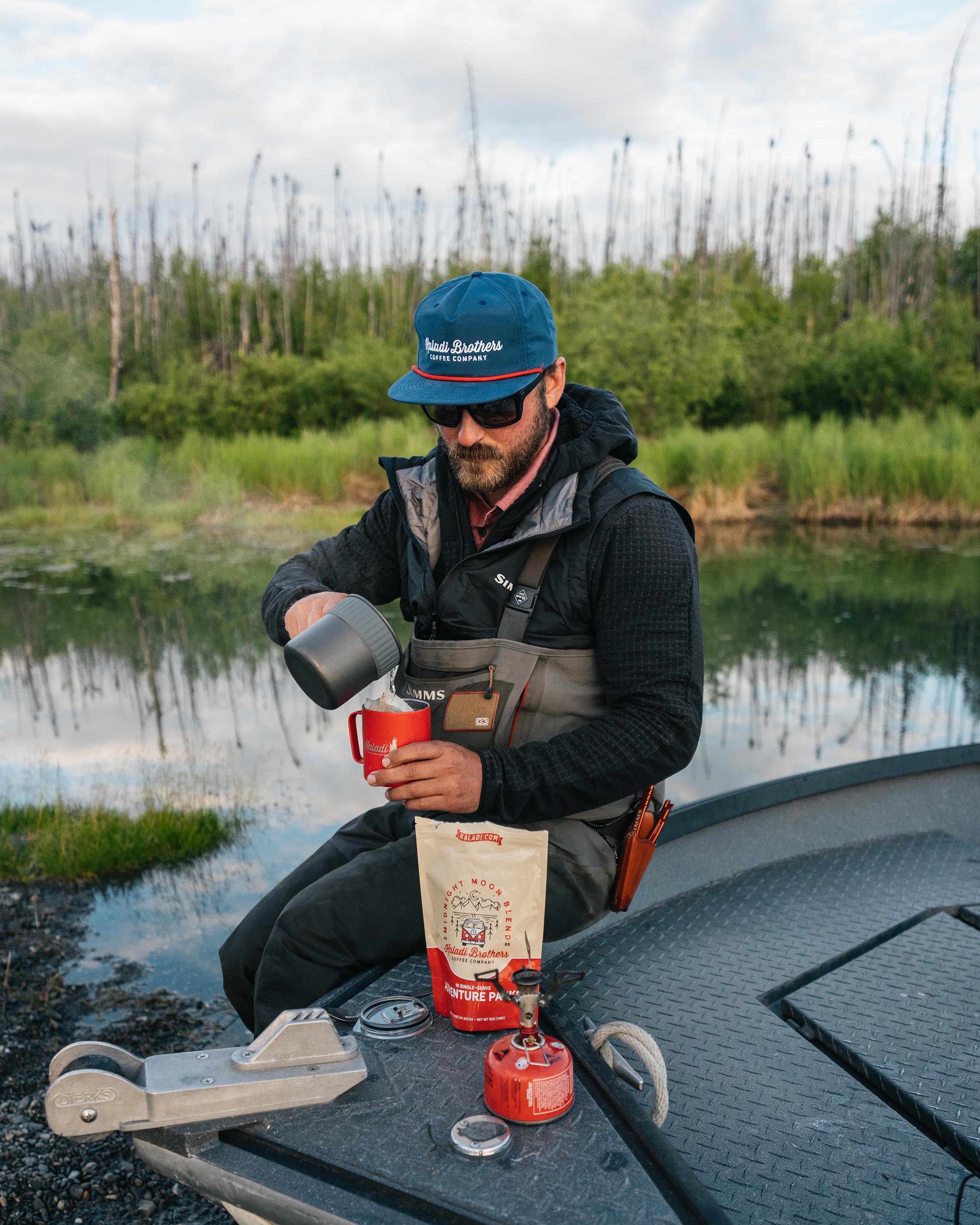 Man brewing Kaladi coffee on a boat beside an Alaska river