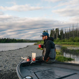 Camper making coffee with a Kaladi Adventure Pack on a riverside boat