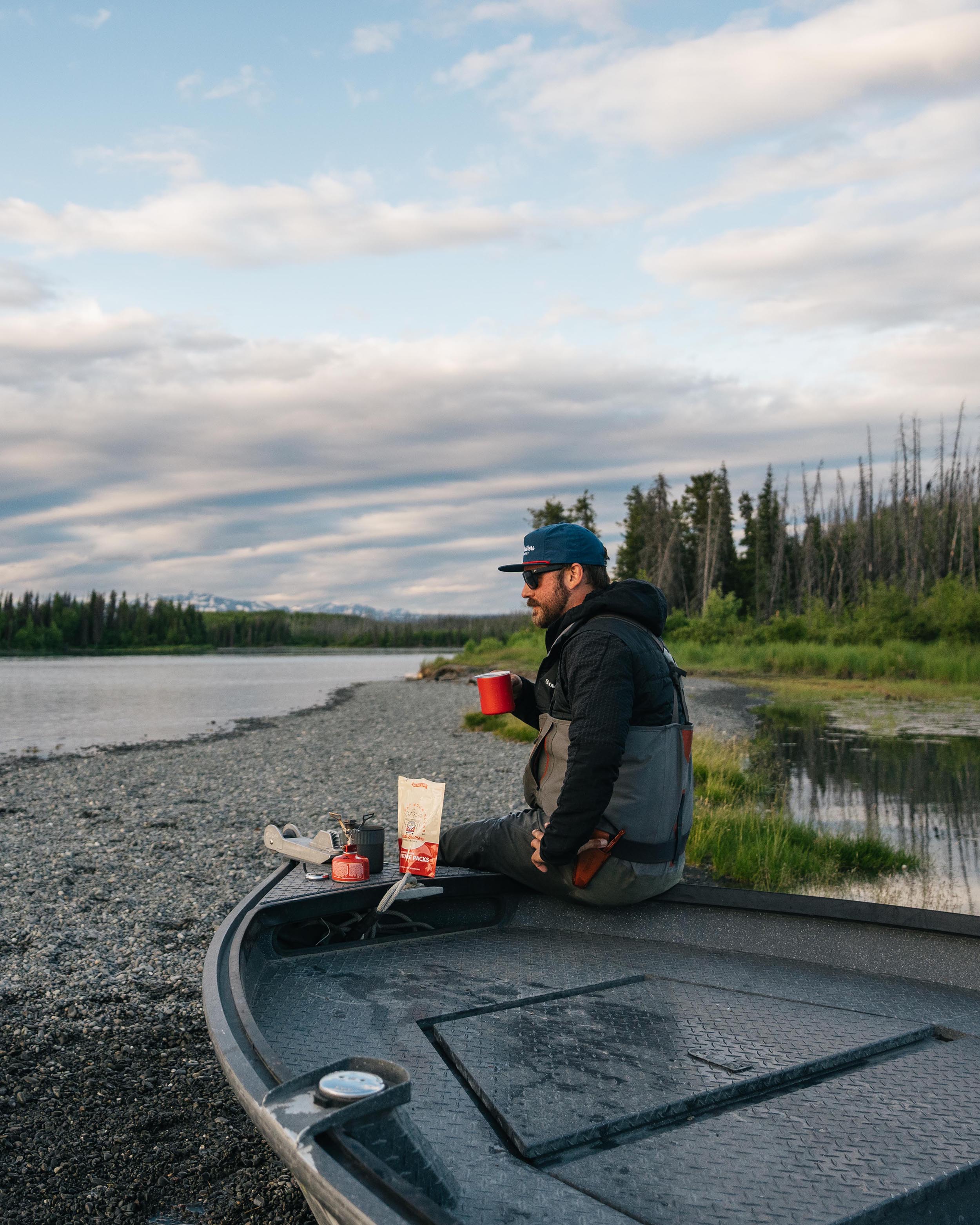 Camper making coffee with a Kaladi Adventure Pack on a riverside boat