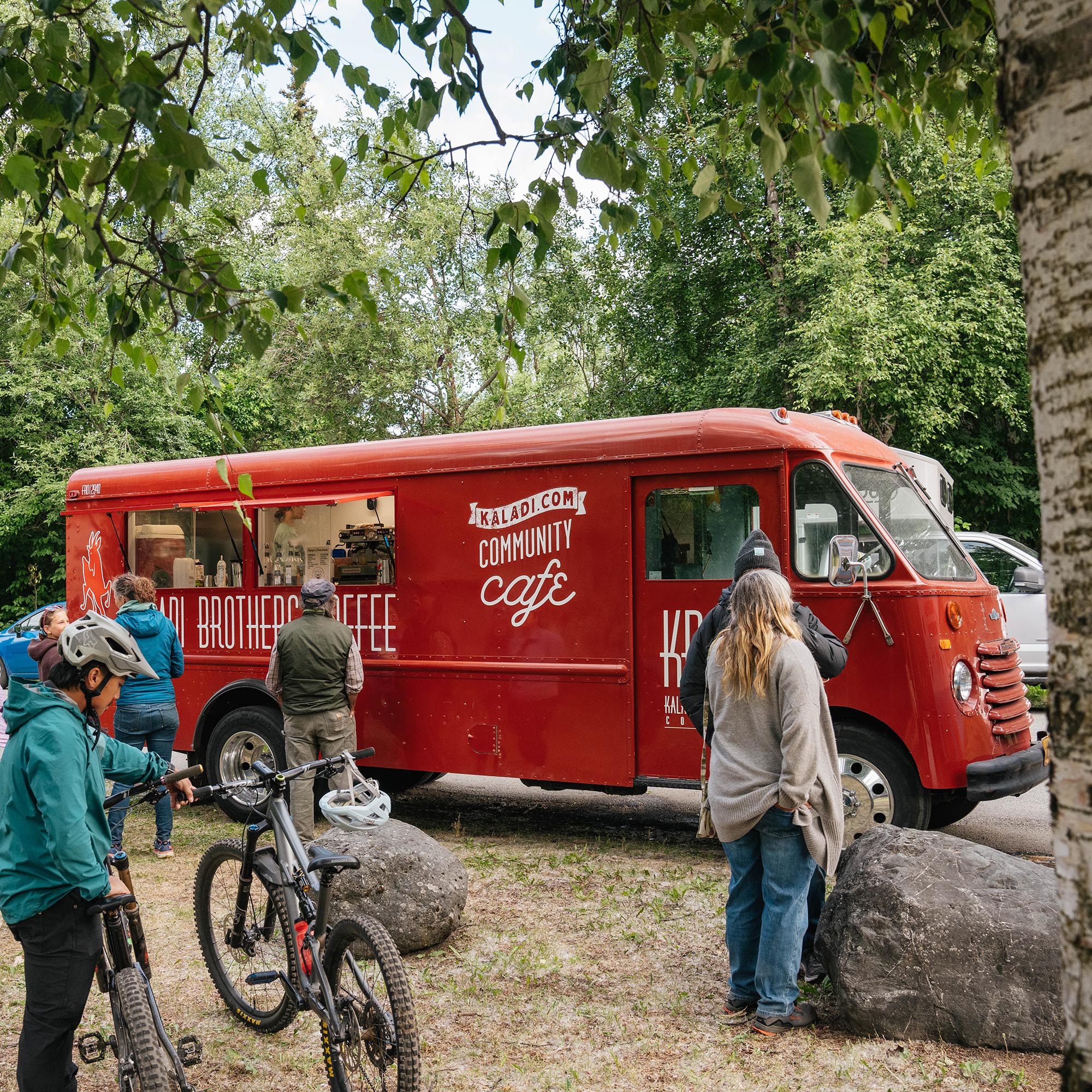 Red community cafe truck in a forest setting with people around
