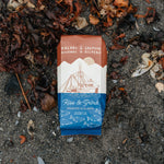Kaladi Brothers & Salmon Sisters coffee package on a sandy surface with seaweed