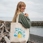 Woman on a rocky beach carrying the Salmon Sisters canvas tote