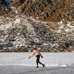 Person ice skating on a frozen mountain lake wearing a Kaladi beanie