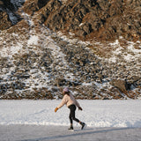 Person ice skating on a frozen mountain lake wearing a Kaladi beanie