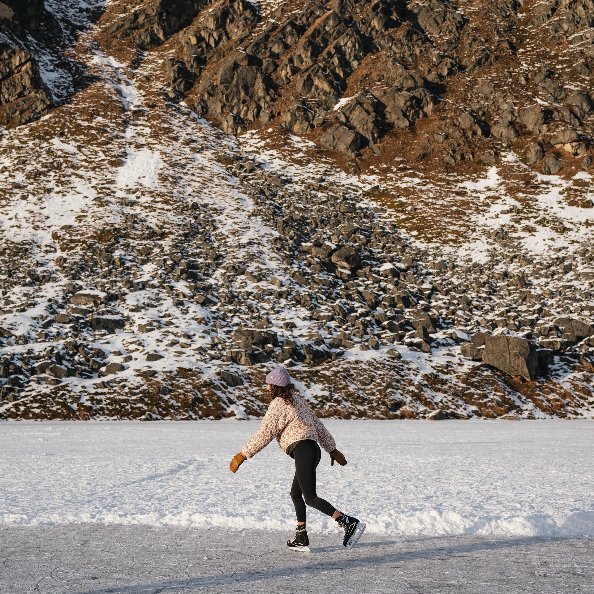 Person ice skating on a frozen mountain lake wearing a Kaladi beanie