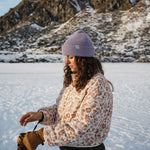 Person wearing a lavender Kaladi beanie beside a frozen lake