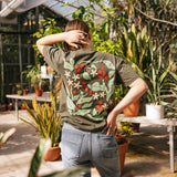 Person wearing a green t-shirt with floral patterns in a greenhouse setting