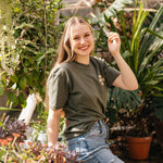 Woman wearing the olive Coffee Cherry T-Shirt in a greenhouse