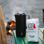 Black MiiR French press and Kaladi coffee bag on a green camp table