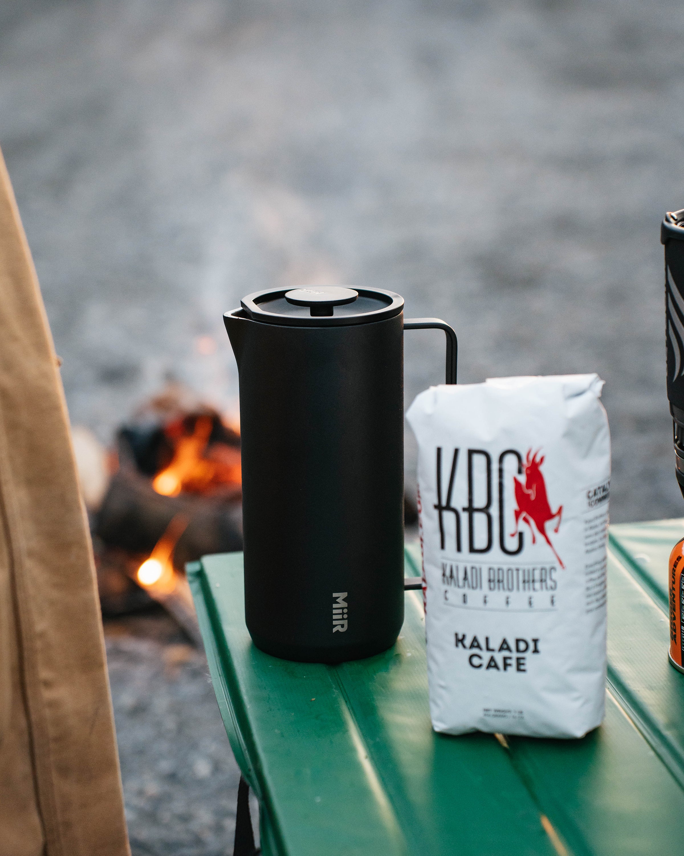 Black MiiR French press and Kaladi coffee bag on a green camp table