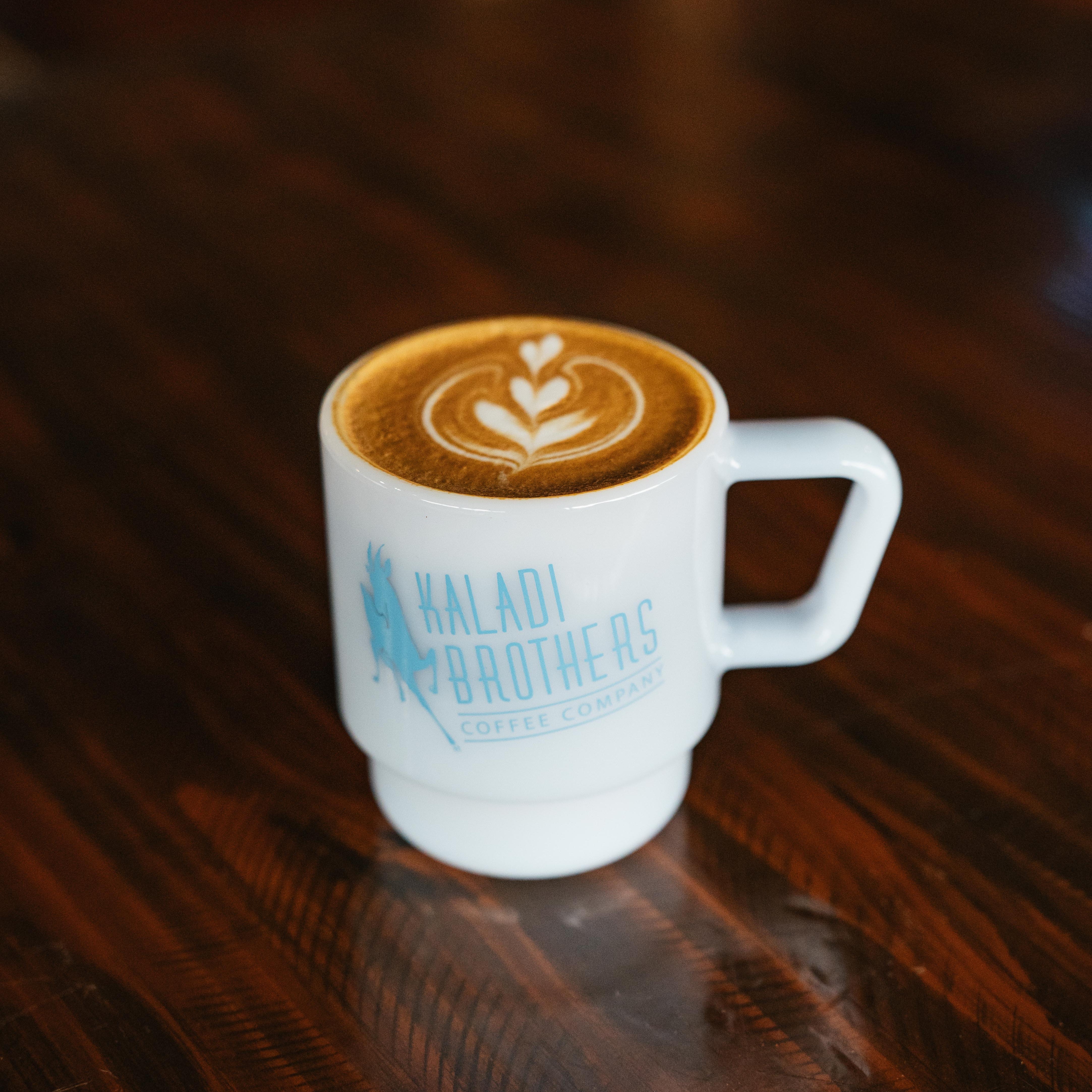 Kaladi milk glass mug with latte art on a wooden table