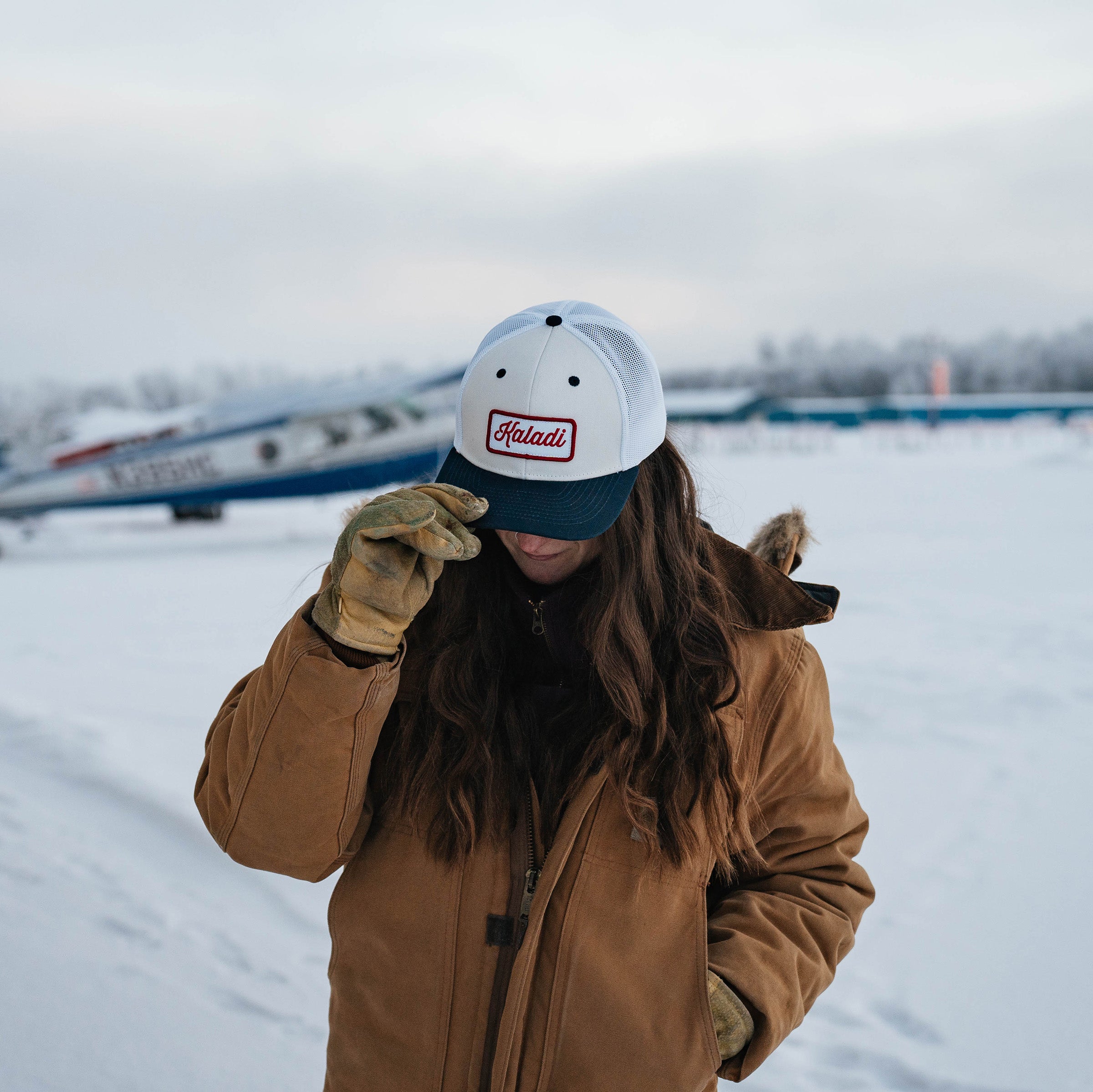 Person wearing the white and navy Kaladi trucker hat in the snow