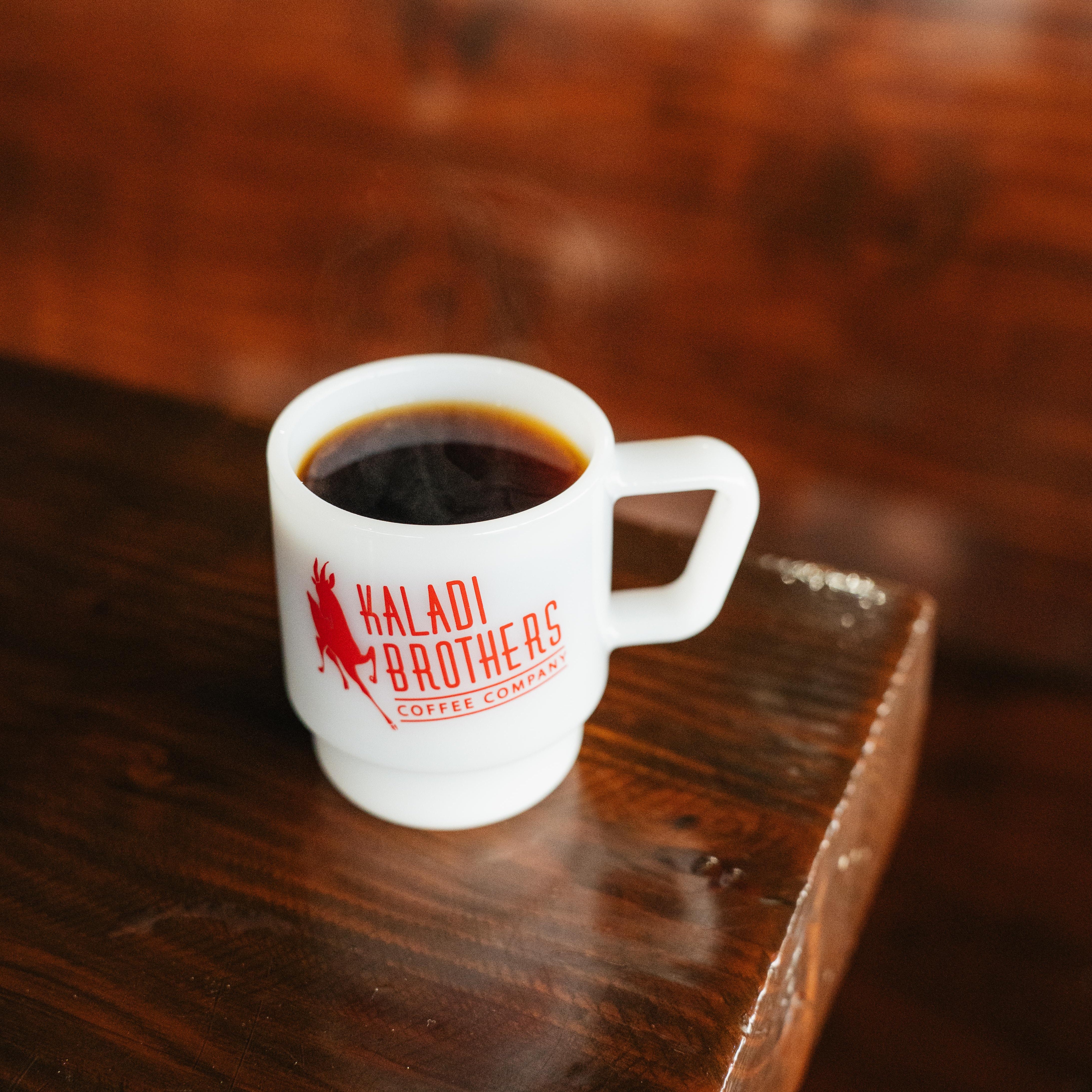 White 8oz milk glass mug of black coffee with red Kaladi logo