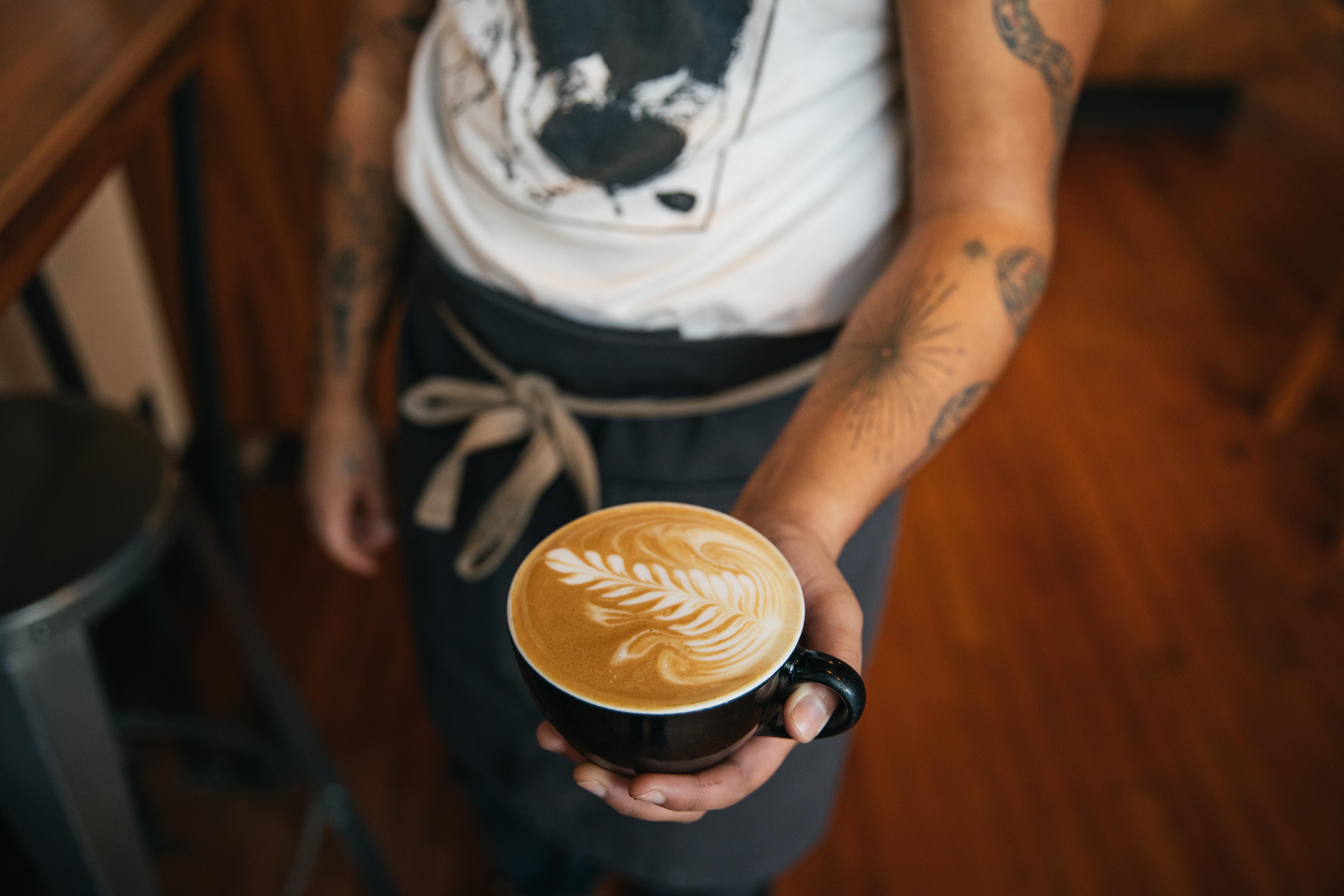 Person holding a cup of coffee with latte art in a casual setting