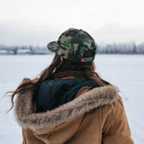 Woman in a fur-lined coat and Kaladi camo hat looking toward snowy mountains