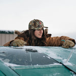 Woman in the Red Goat camo hat leaning on a frosted truck windshield