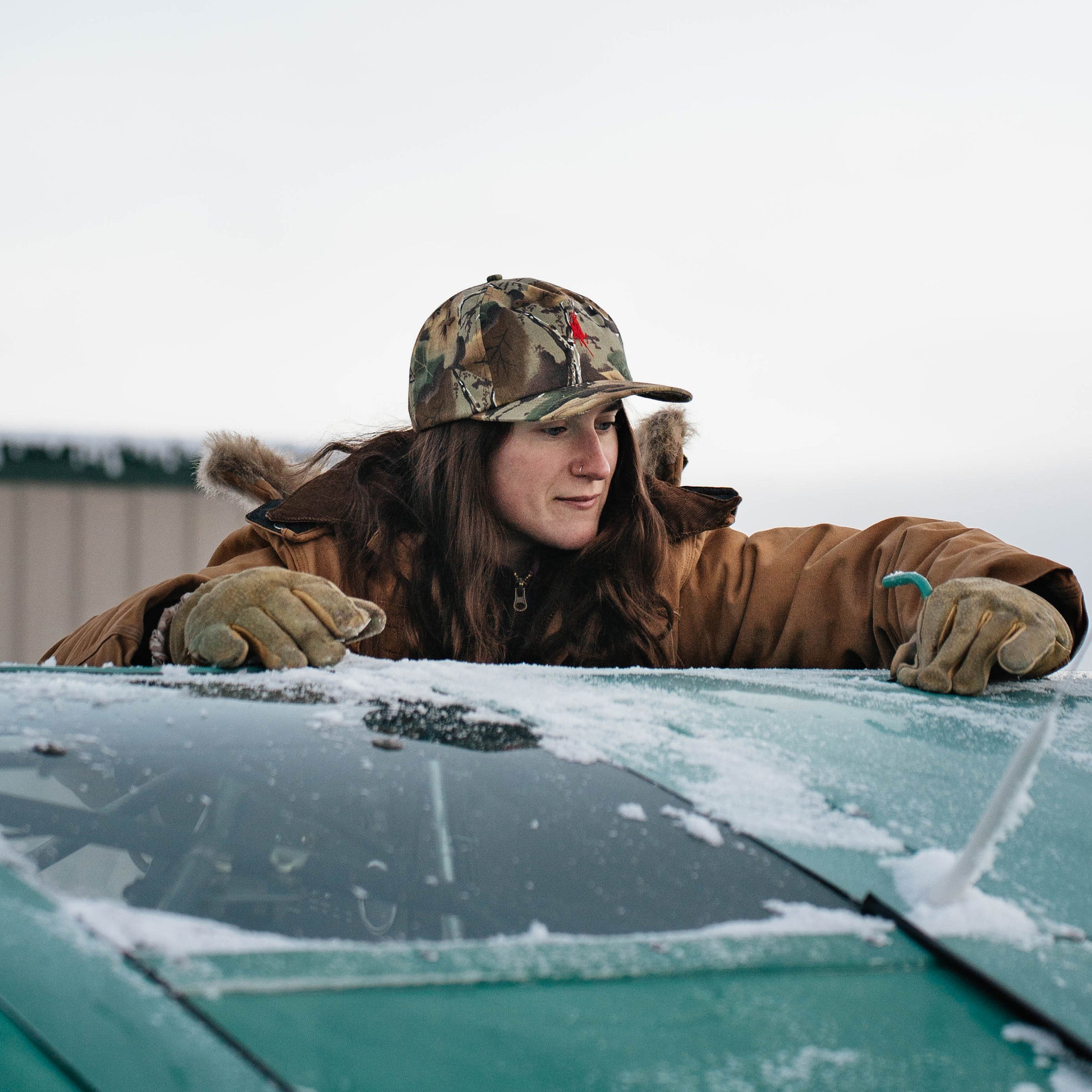 Woman in the Red Goat camo hat leaning on a frosted truck windshield