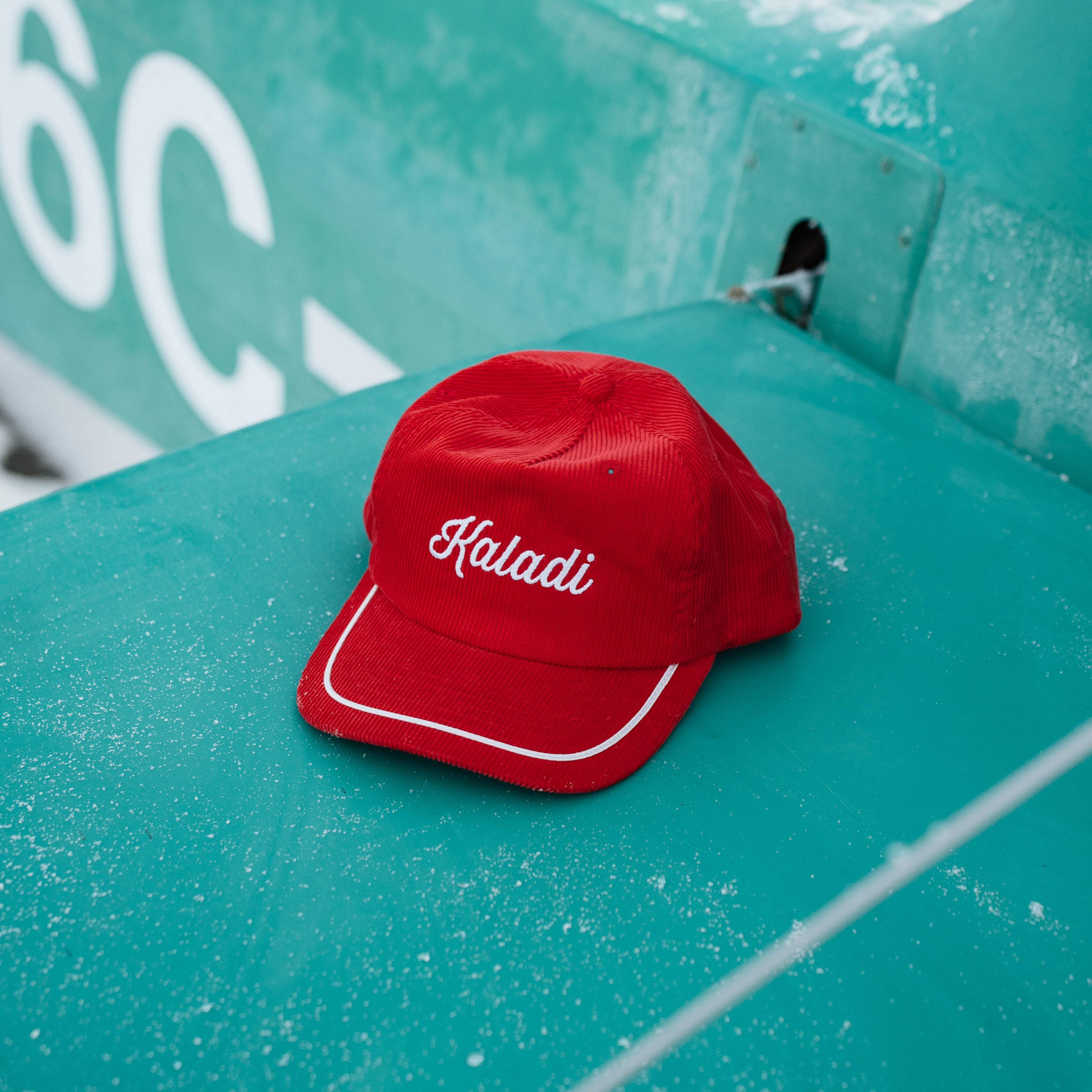Red corduroy Kaladi hat resting on a teal surface