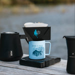 Coffee brewing setup with a blue mug, black filter holder, and black thermos on a wooden surface.