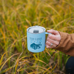 Person holding a blue mug with a design in a grassy field
