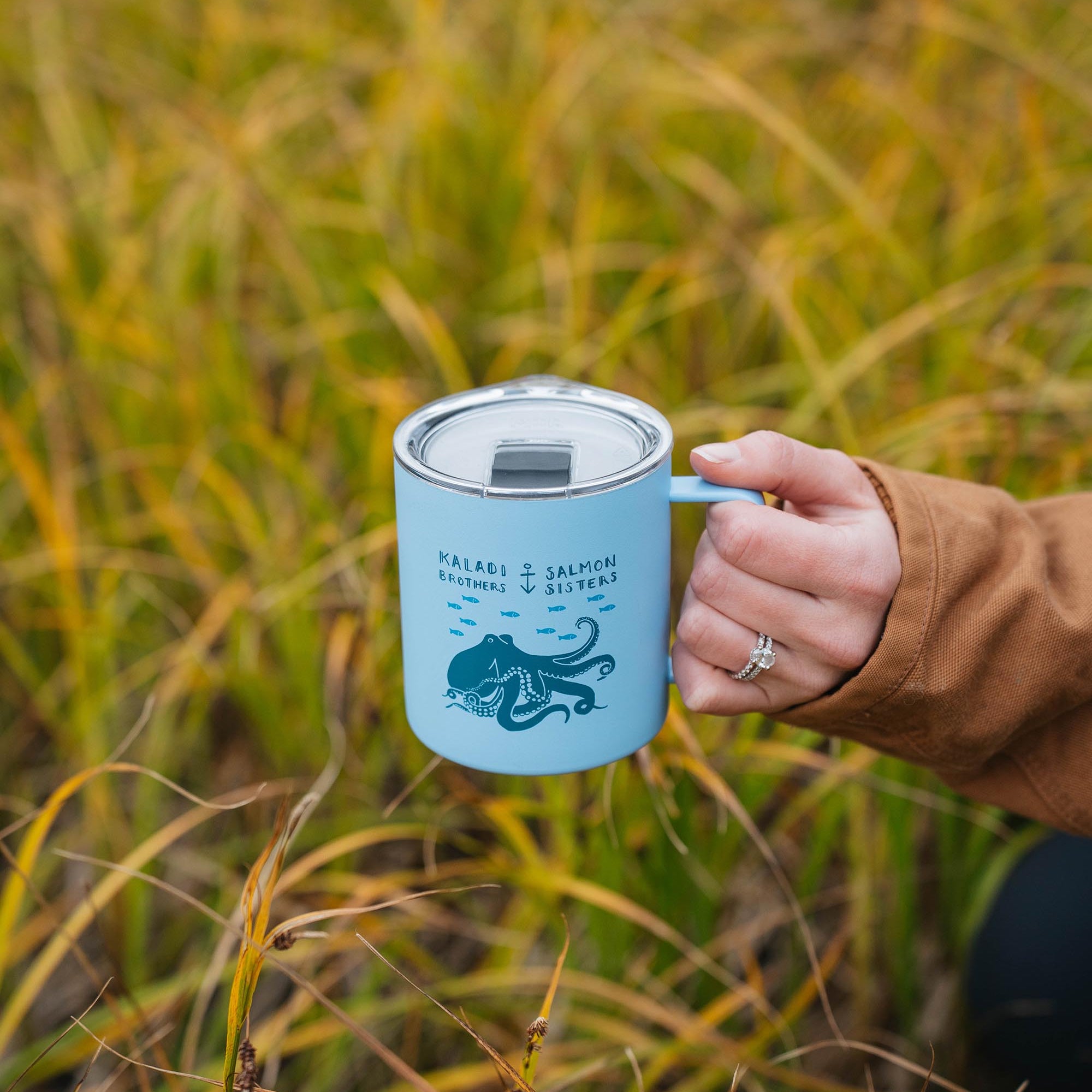 Person holding a blue mug with a design in a grassy field