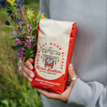 Person holding a red Midnight Moon Blend coffee bag with a bouquet of wildflowers