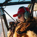 Woman wearing the red Kaladi corduroy hat and aviator headset in a small plane cockpit