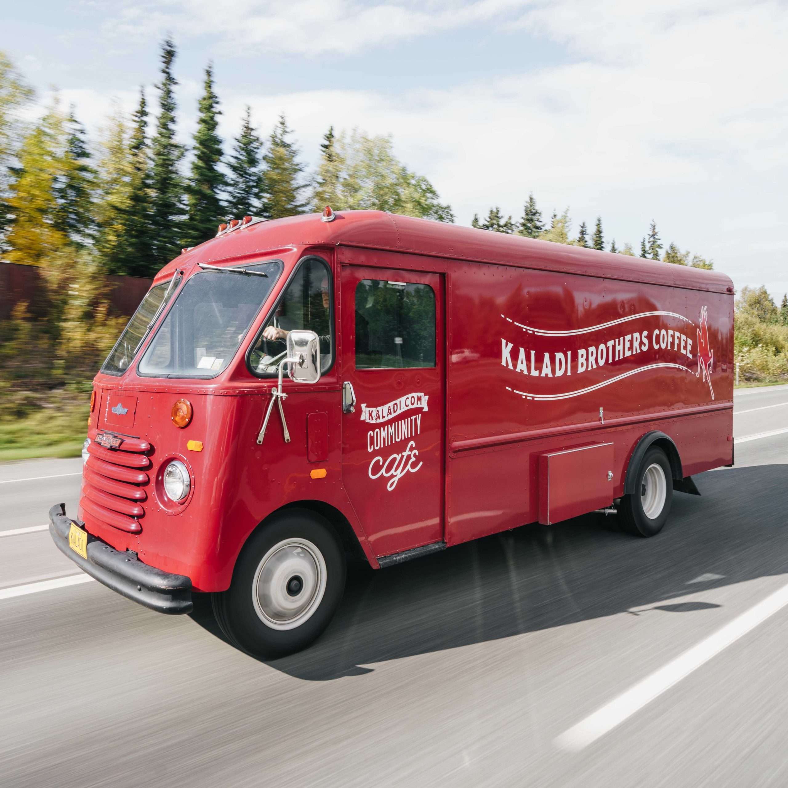 Red Kaladi Brothers Coffee truck driving on a road with trees in the background